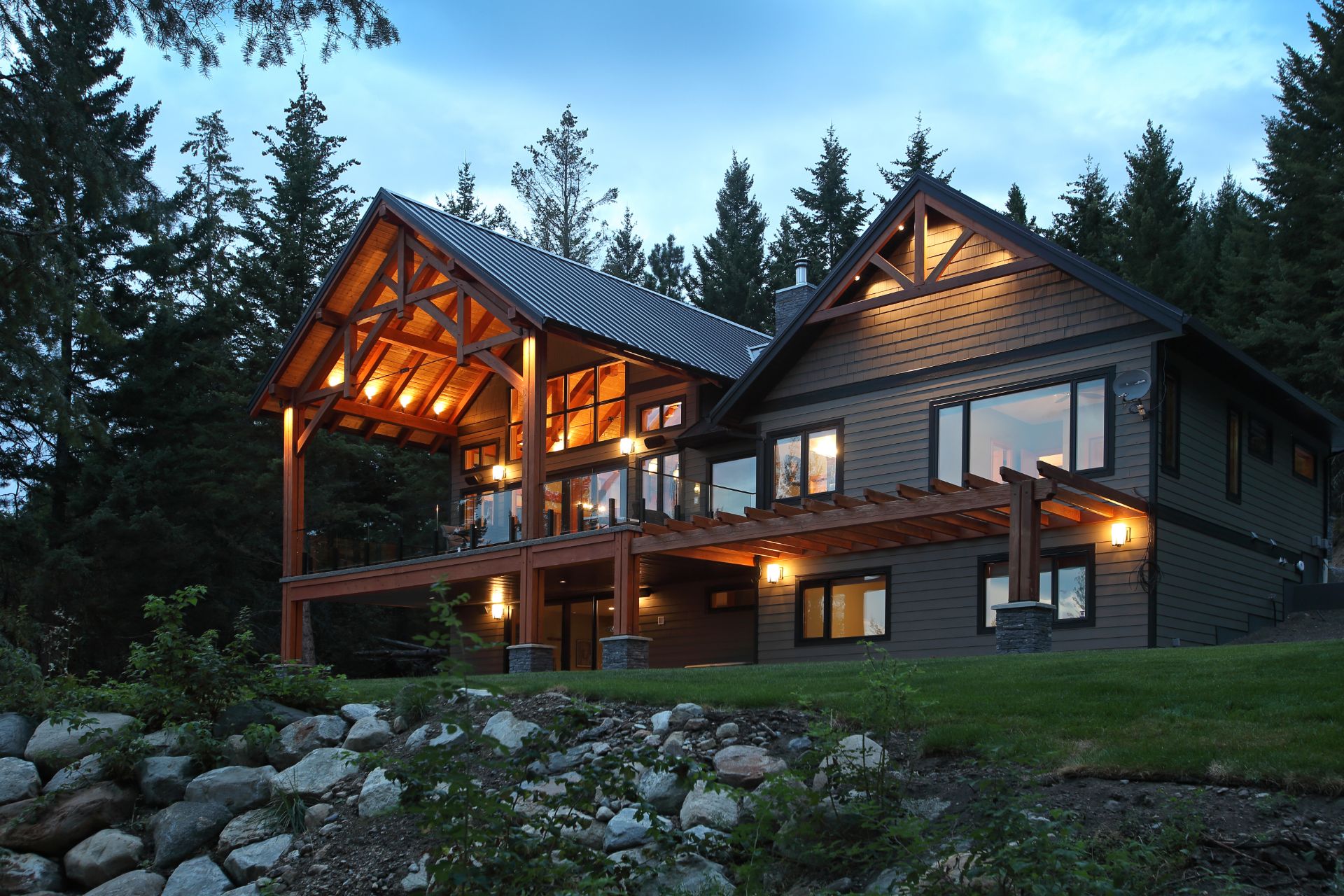 Picture of timber frame home at dusk with interior and porch lights on.