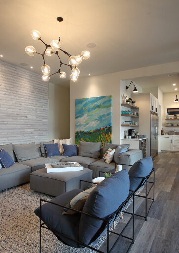 Photo of living room with grey sectional sofa with blue cushions and tongue and groove feature wall.