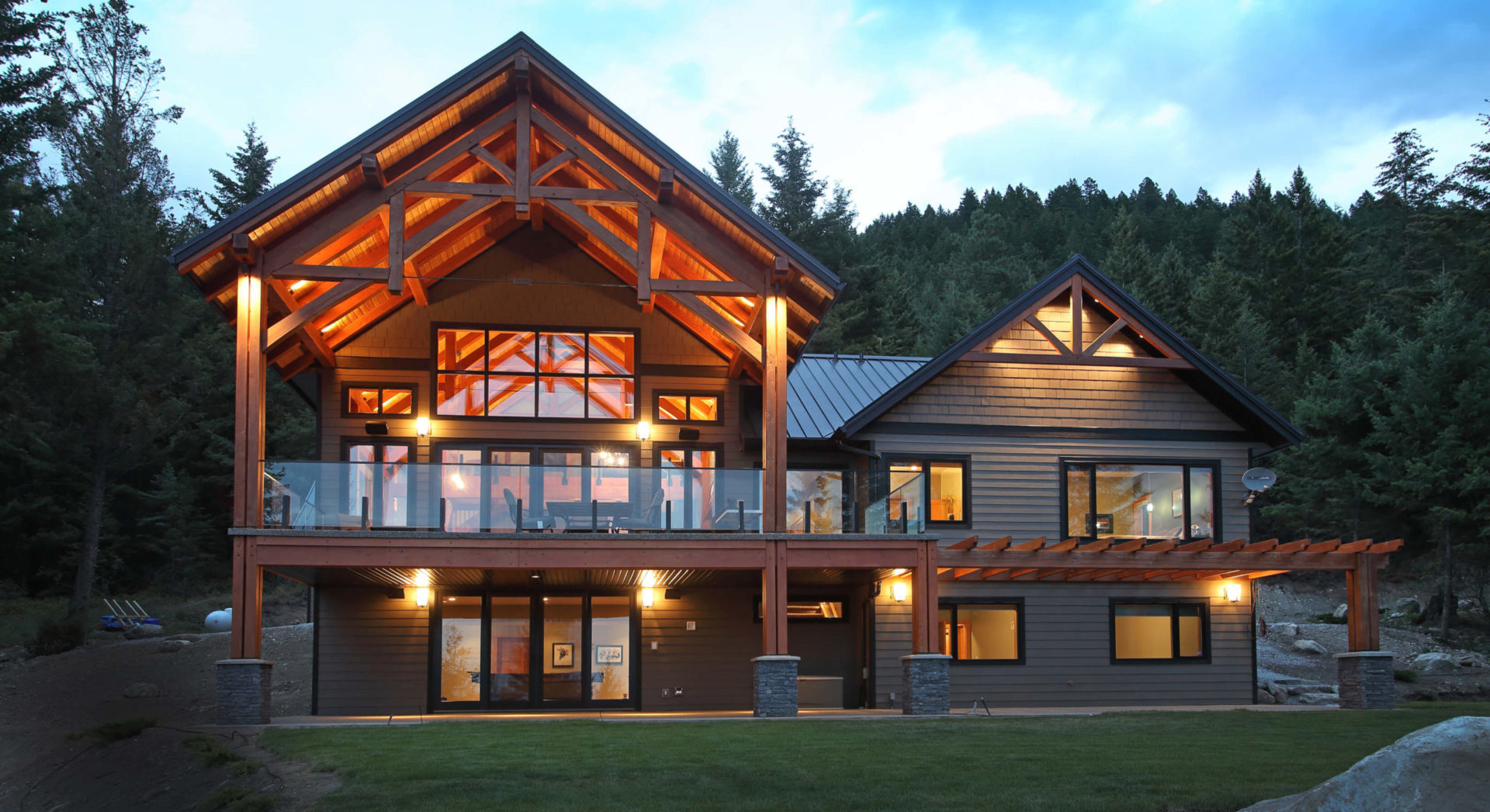 Photo of the front of a beautiful timber frame home at dusk with interior and exterior lights on.